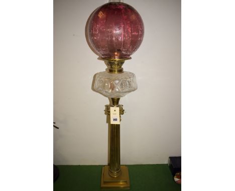 A late 19th Century brass oil lamp, with cranberry tinted floral shade and corinthian column stand.