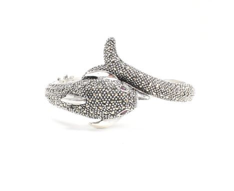 A contemporary white metal and marcasite novelty dolphin bangle having ruby set eyes. Weight approx 54.6g. Measures approx 7c