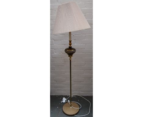 A floor lamp with a circular wooden base and a brass colum with floriate finials and a rounded insert of light brown glass wi