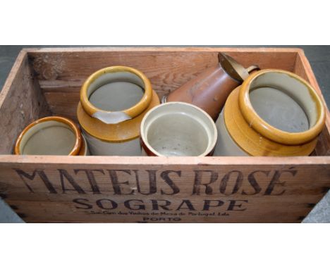 Four stoneware jars of varying sizes and a brass oil can in a wooden wine crate