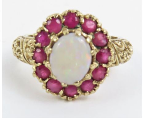 A 9ct gold opal and ruby cluster ring, the oval opal surrounded by twelve round rubies, with heavily decorated shoulders, fin