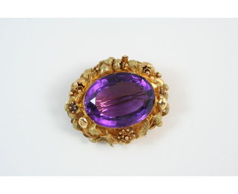 AN AMETHYST AND GOLD BROOCH the oval-shaped amethyst is set within an ornate floral gold surround, 4.5cm. wide.