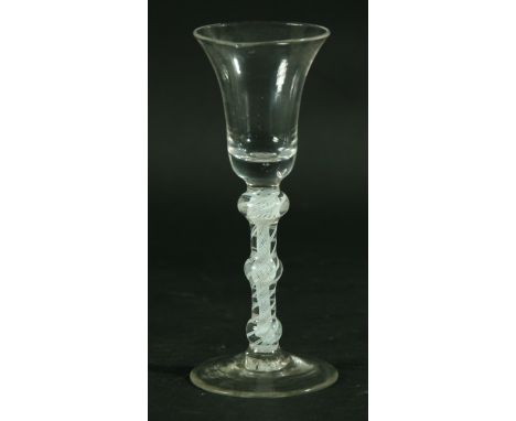 AN EIGHTEENTH CENTURY WINE GLASS, the bell shaped bowl above a triple knopped, white enamel stem with a central gauze inside 