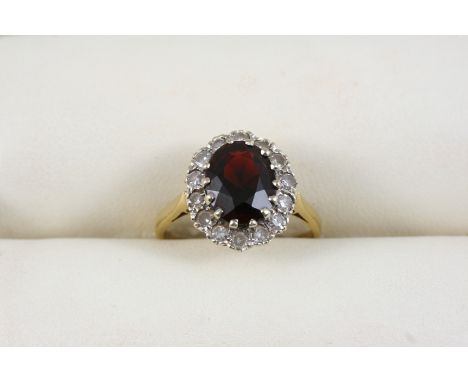 A GARNET AND DIAMOND CLUSTER RING the oval-shaped garnet is set within a surround of single-cut diamonds, in 18ct. gold. Size