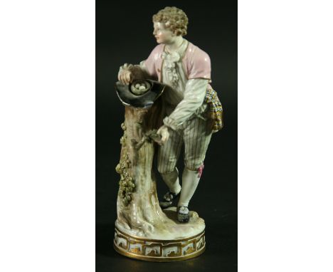 A MEISSEN FIGURE, late 19th century, model 122, of a young man standing by a tree trunk with a nest of eggs in a hat, blue cr