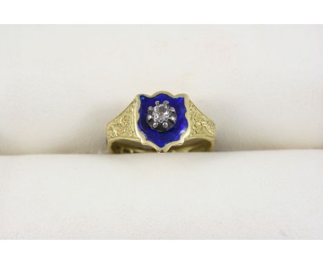 AN ENAMEL AND DIAMOND MEMORIAL RING the blue enamel shield is centred with a cushion-shaped diamond, with gold floral engrave