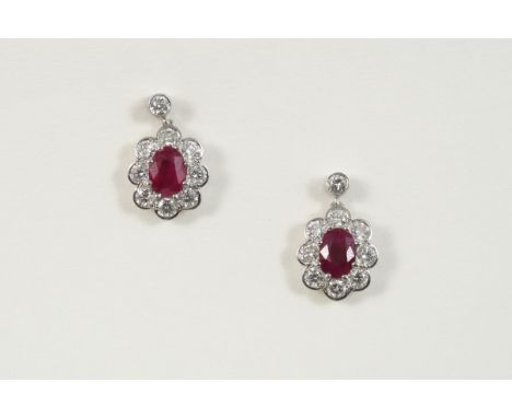 A PAIR OF RUBY AND DIAMOND CLUSTER DROP EARRINGS each centred with an oval-shaped ruby within a surround of eight circular-cu