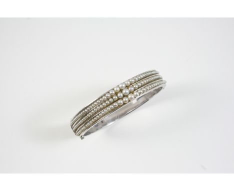 A CULTURED PEARL AND GOLD BANGLE the white gold half hinged bangle is set to one side with three rows of graduated cultured p