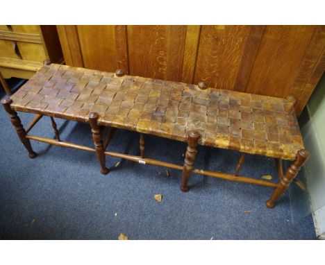An early 20th century Gordon Russell yew wood and woven leather long stool,&nbsp;labelled 'Russell &amp; Sons', 134cm wide. 