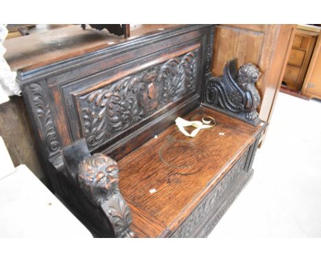 A traditional monks style bench having fixed back and winged lion creature handles , heavily carved throughout , width approx