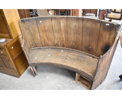 A rustic bench, of curved form, possibly constructed from cut down beer vat or similar, width approx. 140cm