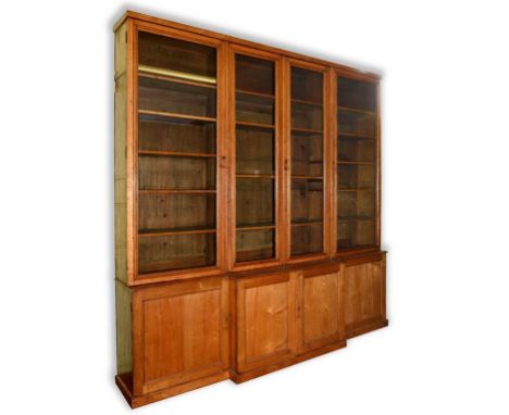 A late Victorian oak and ash breakfront library bookcase, having two pairs of glazed doors above two pairs of panel doors, on