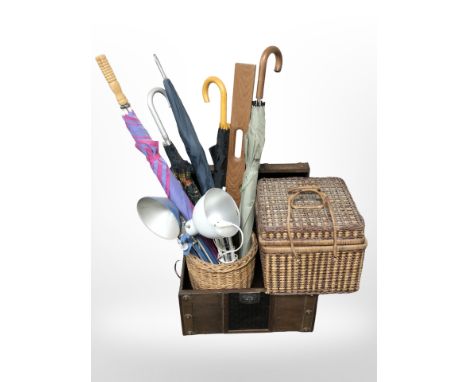 A faux leather trunk containing wicker basket, assorted umbrellas, two angle-poise lamps, and a wicker picnic basket.