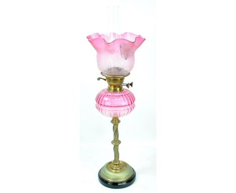 A late Victorian brass oil lamp with wrythen twisted stem, pale cranberry tinted reservoir and pink tinted etched shade, heig