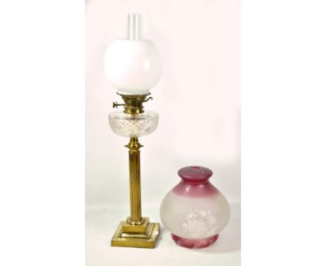 A brass oil lamp with column on stepped square base beneath clear glass reservoir and opaque shade with clear chimney, height