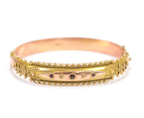 An early 20th century 9ct yellow gold garnet and diamond chip set hinged snap bangle with filigree decoration to the upper ba