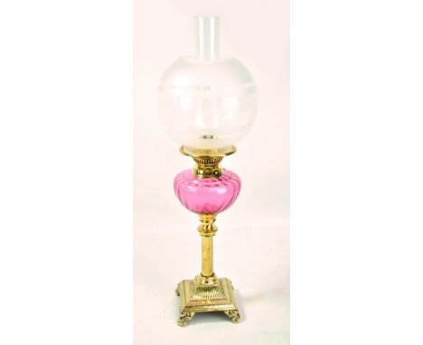 A brass column oil lamp on square footed base, cranberry glass reservoir, associated globular shade with etched detail and cl