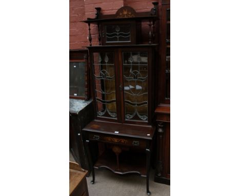 An Art Nouveau mahogany display cabinet with top shelf above single stained glass compartment above a pair of similar doors a