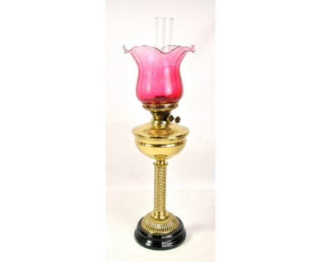 A brass oil lamp with twisted column on circular base with brass reservoir, duplex burner, cranberry shade with crimped rim a