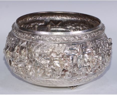 A large Burmese silver metal bowl, repousse chased in bold relief with a hunting scene, deities, an elephant and a procession
