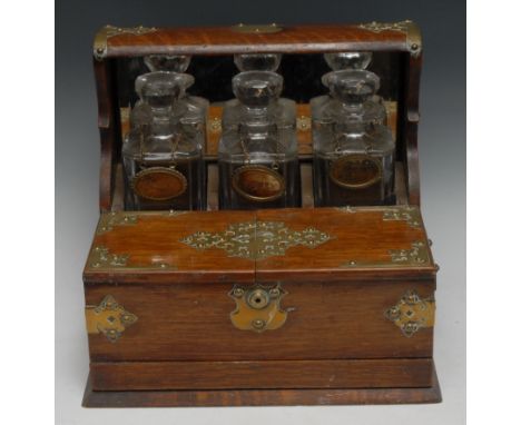 A Victorian oak tantalus, the three decanters restrained within a mirrored niche, hinged twin-covers enclosing provision for 
