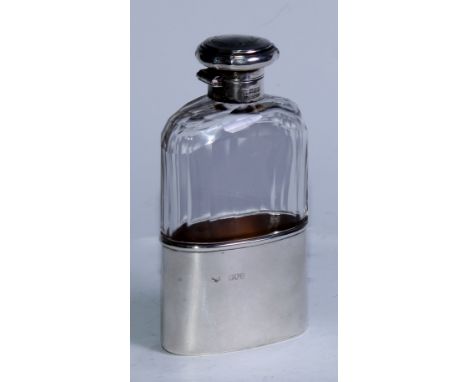 A George V silver and faceted glass hip flask, hinged bayonet cover engraved with a ribbon-tied band of leafy scrolls, stirru