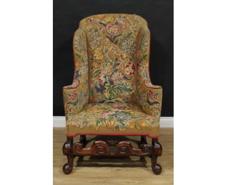 A 19th century wingback armchair, in the William and Mary taste, shaped back, outswept arms, stuffed-over tapestry upholstery