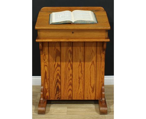 A Victorian pitch pine schoolmaster's desk, hinged sloping top, fitted brass inkwell slide, the base with rectangular panel d