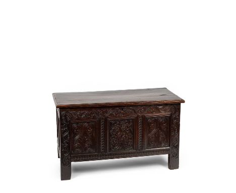 A Charles I oak panelled chest, the plank lid above a three panel front, carved with scrolling foliage below a trailing vine 