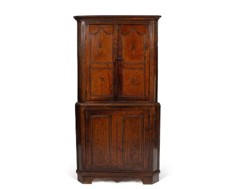 A George IV oak standing corner cupboard, the moulded cornice and dentil frieze above two shaped panelled doors, within reede