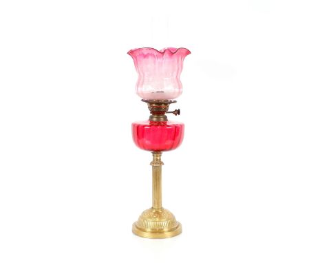 An oil lamp with embossed brass base and Corinthian column, cranberry glass reservoir and etched ruby shade