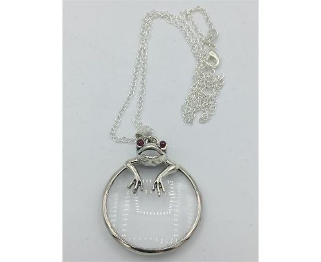 A silver magnifying glass in the form of a frog with ruby eyes