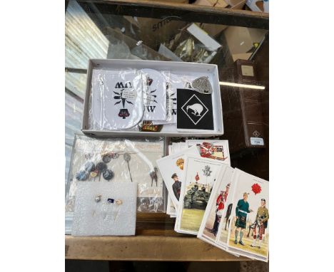 A box containing sew on badges, a collection of postcards, all showing military outfits, and a small collection of stick pins