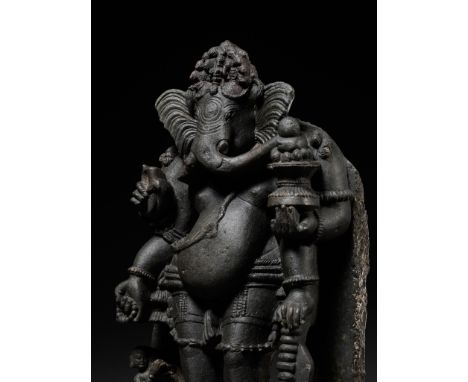 A GRANITE FIGURE OF GANESHA, ORISSA, 13TH CENTURYStanding in sambhanga on a lotus pedestal with a female worshipper kneeling 