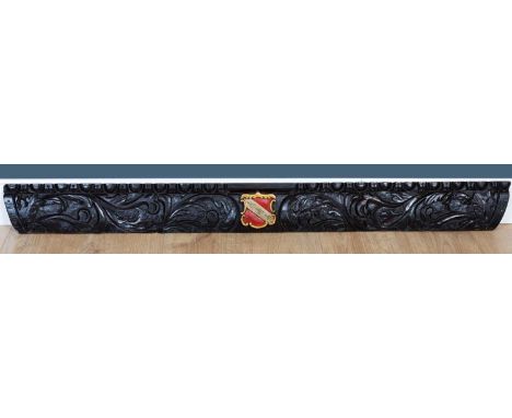An oak carved architectural element, with a central red and gold painted shield, 124.5cm wide x 1cm deep x 13cm highCondition