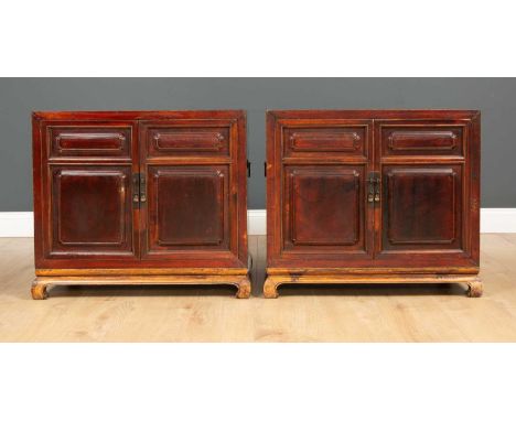 A pair of Chinese low cabinets each with panelled doors opening to reveal a shelf with two drawers and all on a stand with sc