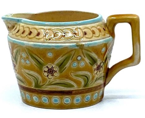 A small Linthorpe Pottery milk jug, pale treacle glaze with blue dots and lines and a band of green and white stylized foliag