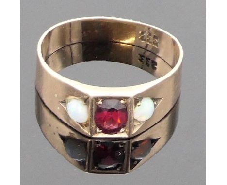 A yellow metal ring set centrally with a garnet 6mm x 4mm, and a small round opal to either side, the plain band shank stampe