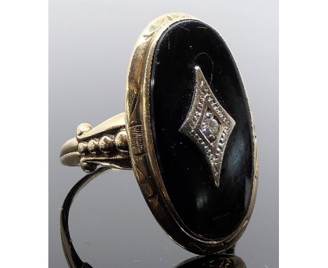 A yellow metal dress ring with a black enamel oval panel (20mm x 11mm) and a very small round cut diamond centrally in a whit