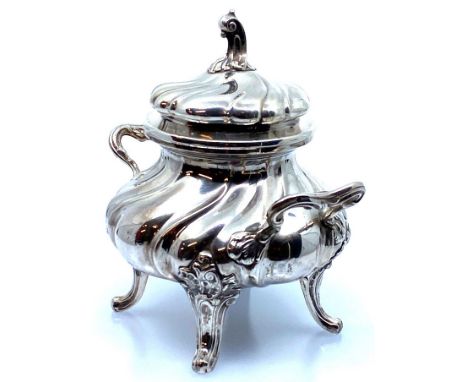 A white metal lidded sucrier bowl of wrythen form with two handles, the lid with a scrolled knop, on four moulded scrolled fe