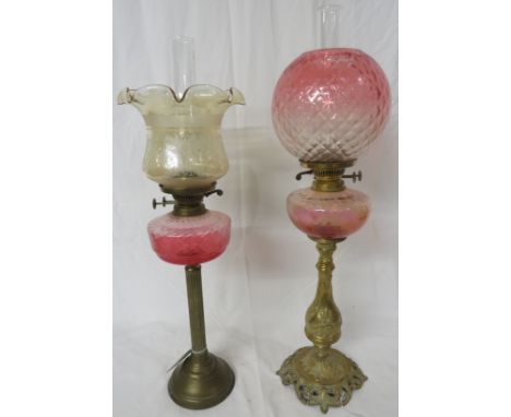 Two brass oil lamps - the first with a reeded column on a stepped circular foot with a ruby glass reservoir and a light amber