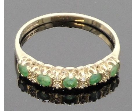 A 9 carat gold ring set with a line of five small emeralds (each about 2.5mm x 2.5mm) spaced by four pairs of chip diamonds, 