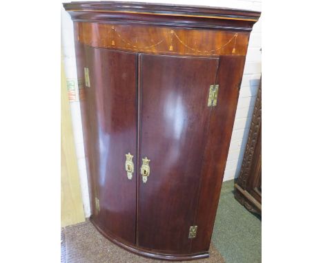 Georgian mahogany bow-fronted wall-mounting corner cupboard, two doors with brass H-hinges and moulded urn and swag escutcheo