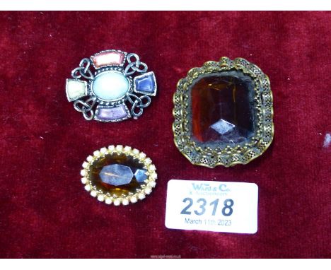 A large brown stone brooch with metal frill surround, plus a smaller one in similar style and a Celtic style brooch.