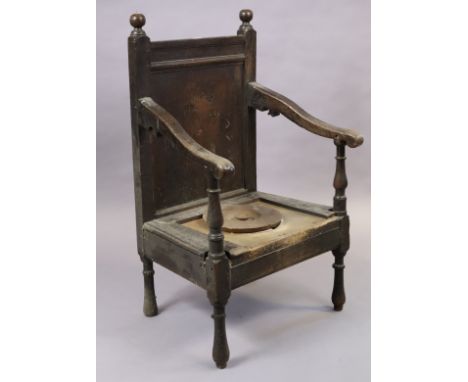 An 18th century joined oak armchair with panelled back, open scroll arms &amp; commode seat, on turned legs.