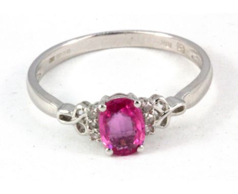 An 18ct white gold ring set with an oval cut pink sapphire and diamond set shoulders, (S).