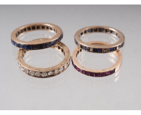 A yellow metal and blue stone eternity ring, a similar yellow metal and clear stone set eternity ring, another eternity ring 