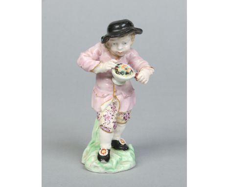 A Derby figure of a boy wearing a brimmed black hat and holding a pan of food. Decorated in coloured enamels and raised on a 