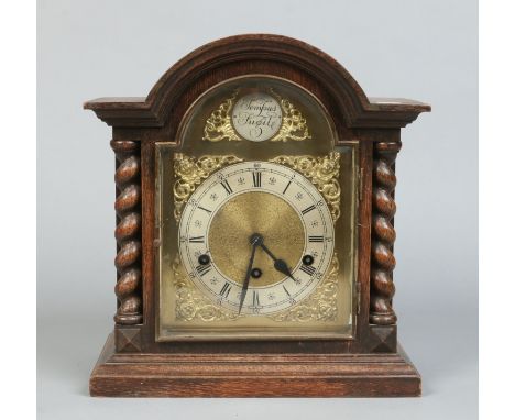 An oak cased eight day Westminster mantel clock with barley twist supports. With brass arch top dial ornamented with spandrel