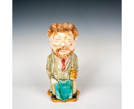 Glazed figural jug with red interior glaze. Features a politician holding a purse of money and a sign with the phrase Reforme